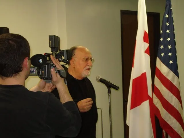 Ushangi Rizhinashvili speaking at a microphone beside the Georgian and American flags