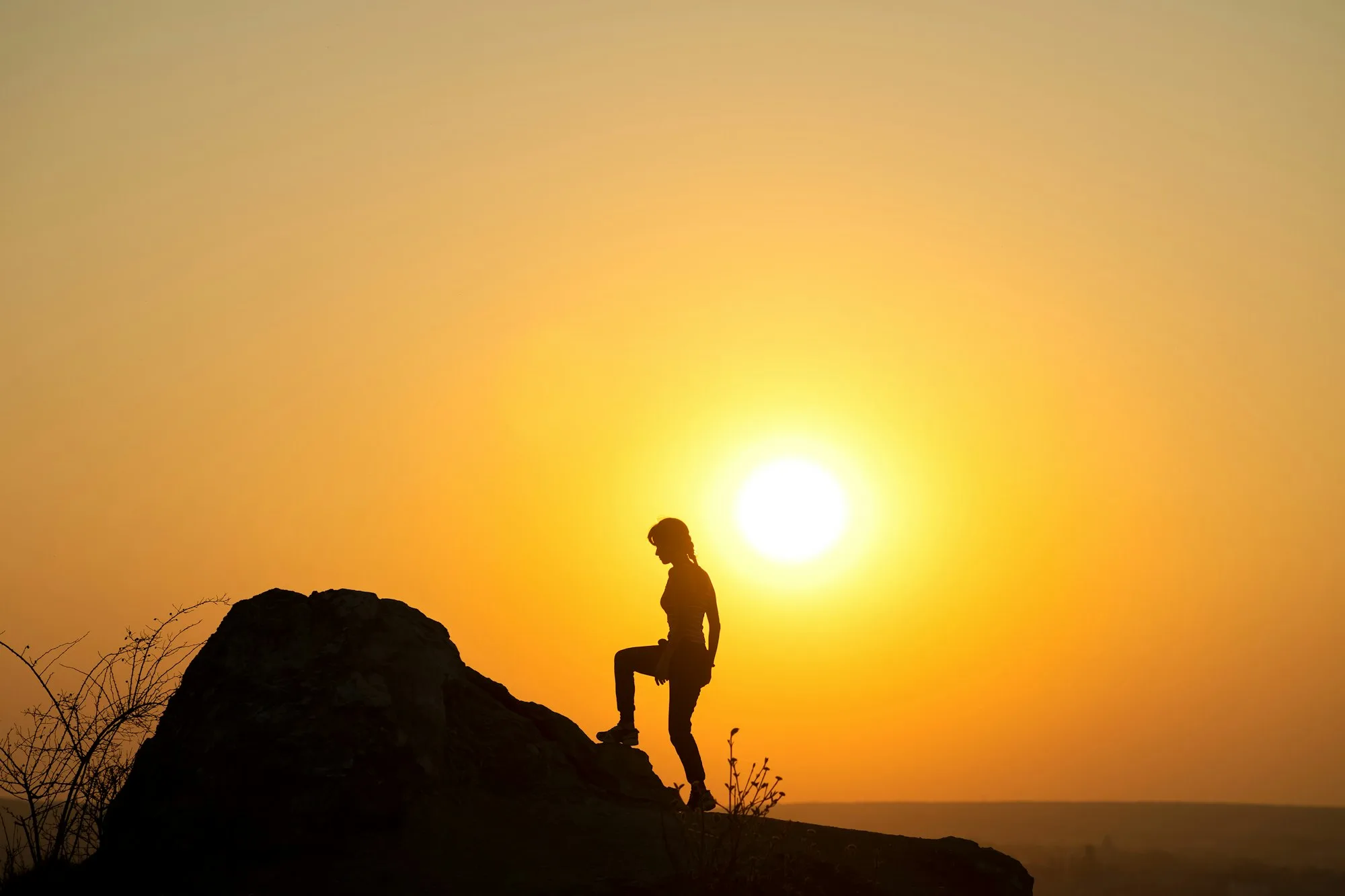 Silhouette of a woman hiker climbing up a big stone at sunset